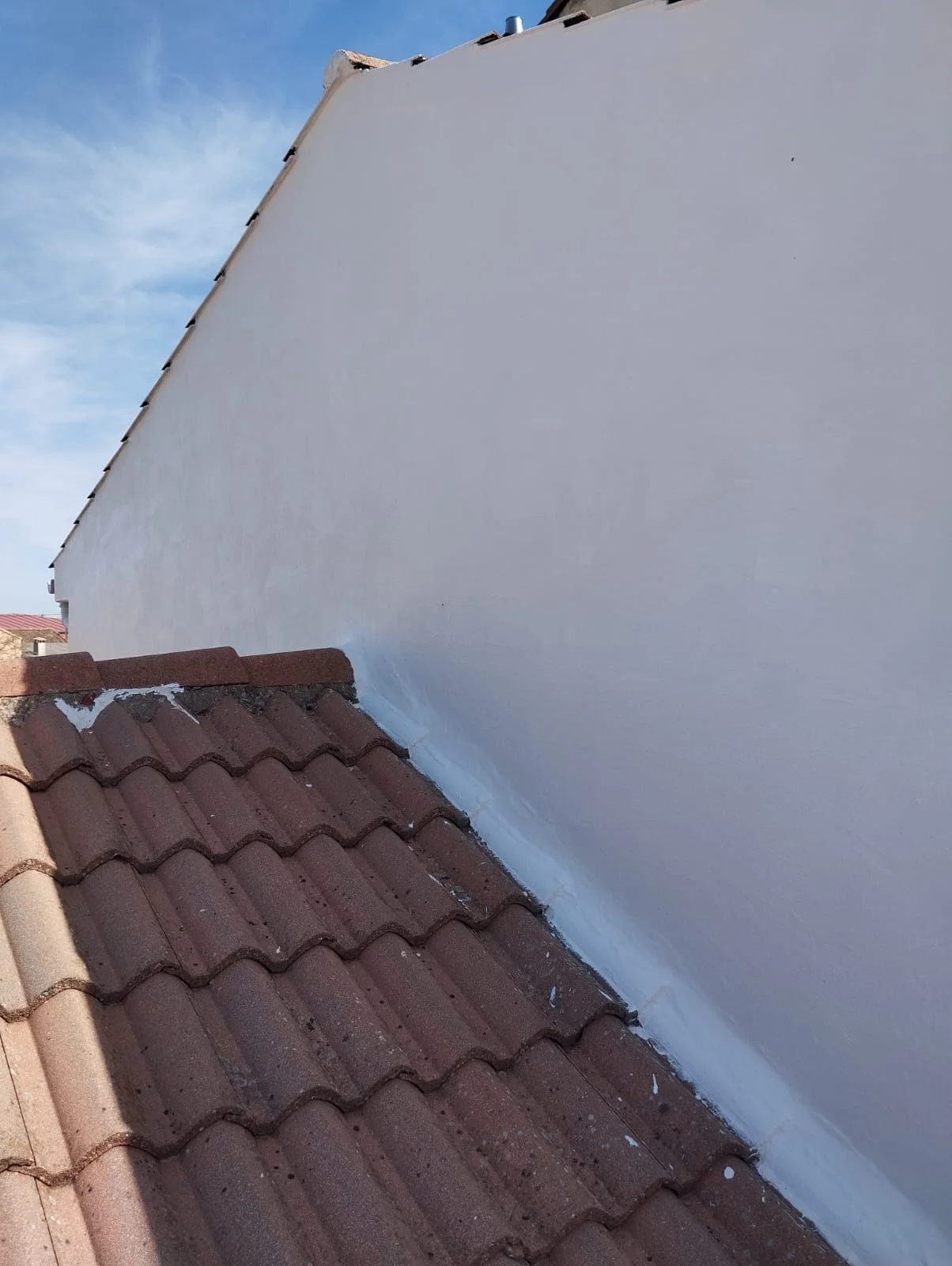 Impermeabilización de fachada en Villabilla, con sellador blanco aplicado en la unión entre la pared y el tejado de terracota